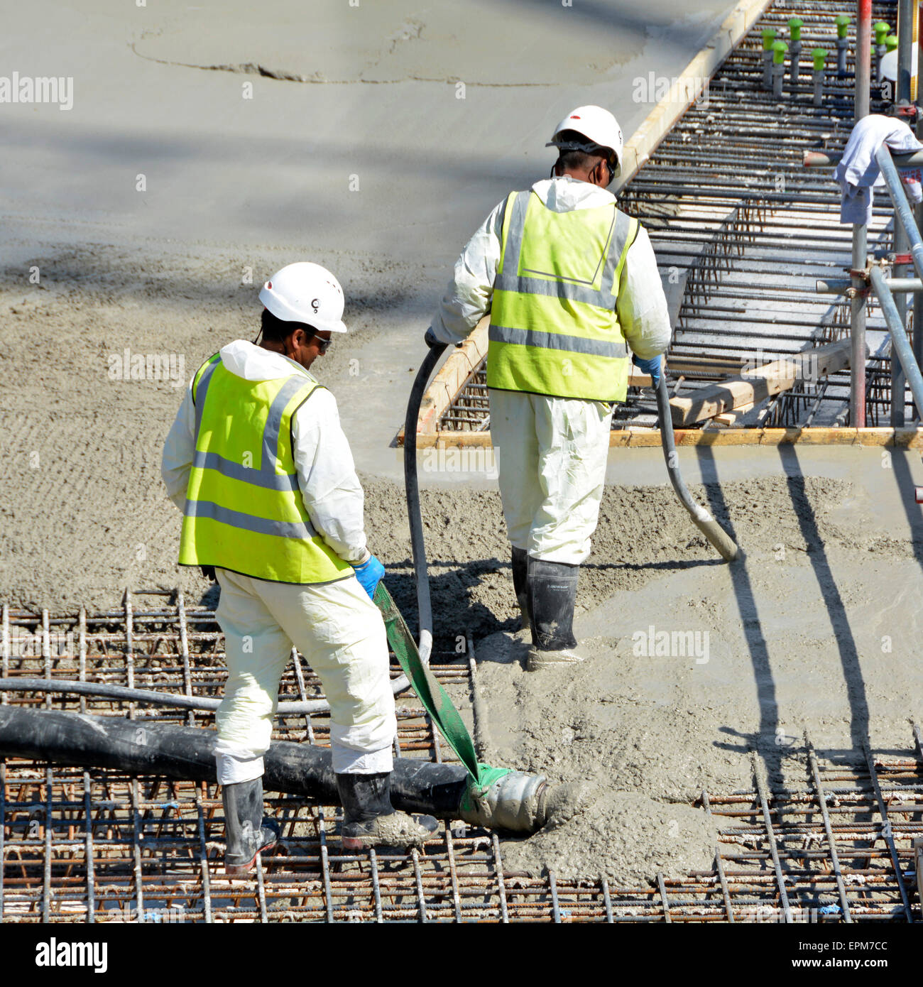 Close up building construction industry site workers placing & vibrating pumping concrete into reinforcement floor slab for apartment block London UK Stock Photo