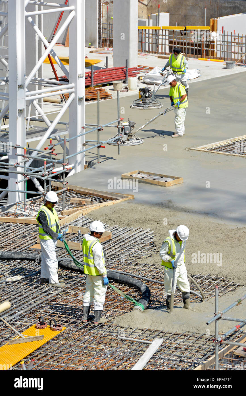 Construction building industry site place & vibrate pumped concrete into reinforcement with power float workers finishing smooth floor slab London UK Stock Photo