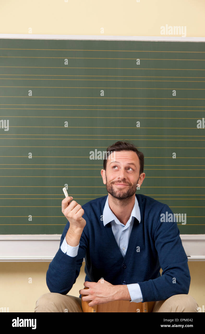 Smiling teacher in classroom at blackboard looking up Stock Photo