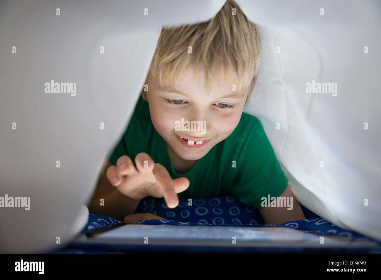 Boy using digital tablet in bed under blanket Stock Photo Alamy