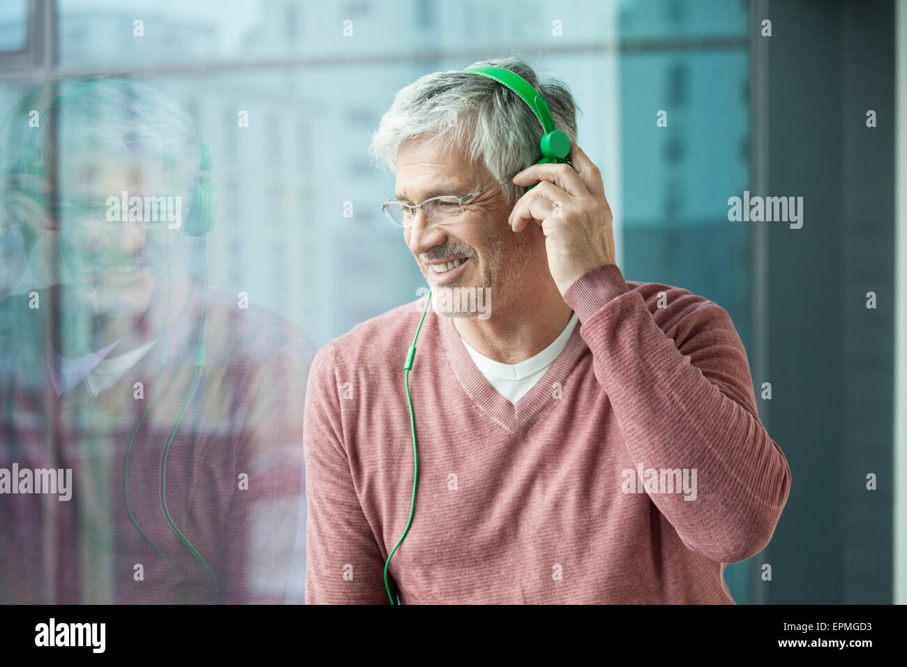 Man with green headphones looking through window Stock Photo