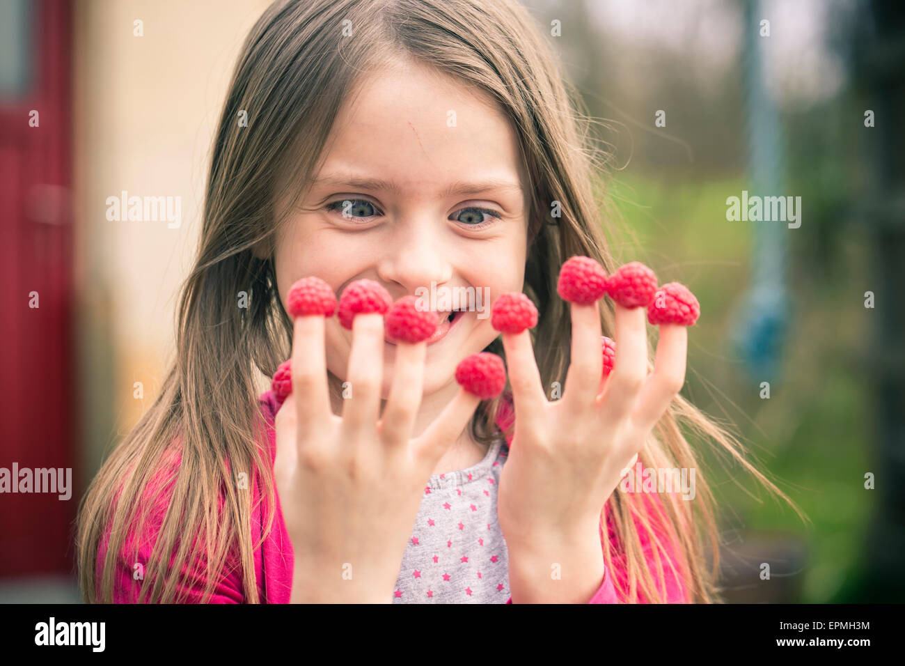 Happy girl with raspberries on her fingers Stock Photo