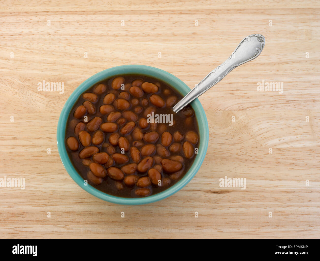 A small bowl filled with country style baked beans with a spoon atop a wood table top. Stock Photo