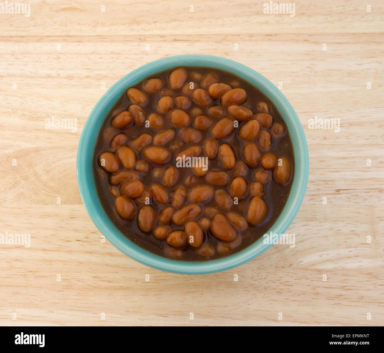 Top view of a bowl filled with country style baked beans on a wood table top. Stock Photo