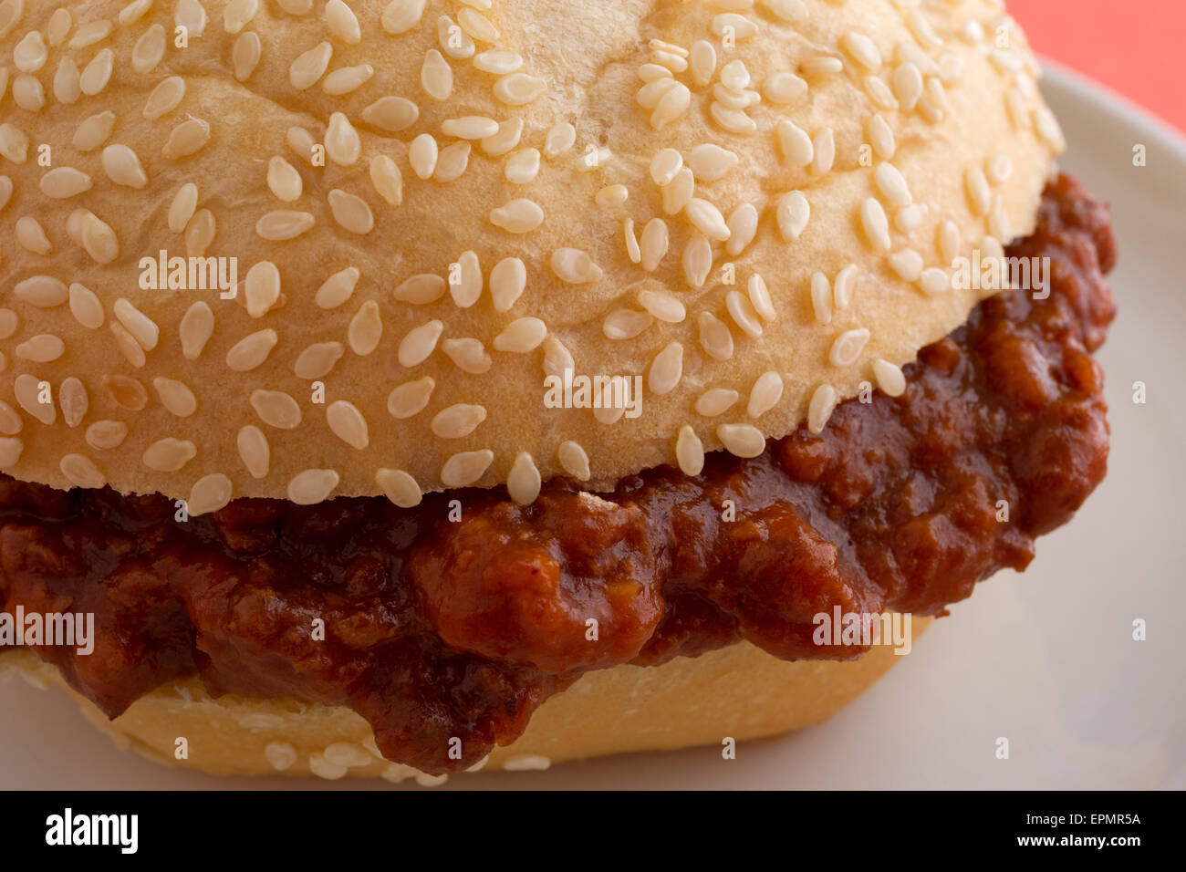 A very close view of a sloppy joe sesame seed roll sandwich on a small