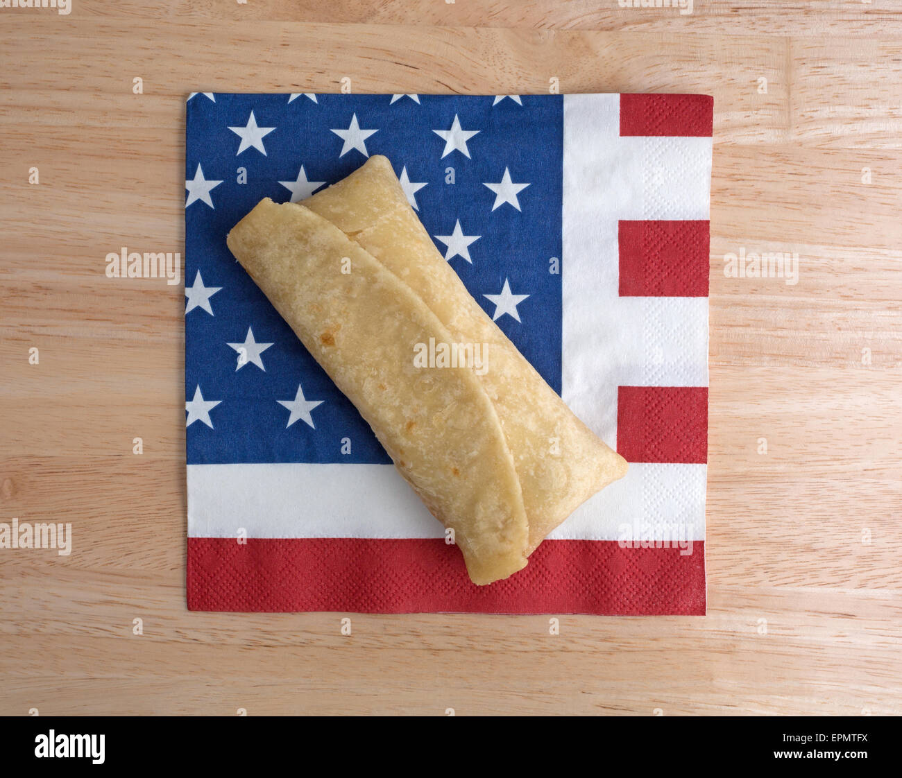 Top view of a microwaved chimichanga on an American flag motif napkin atop a wood table top. Stock Photo