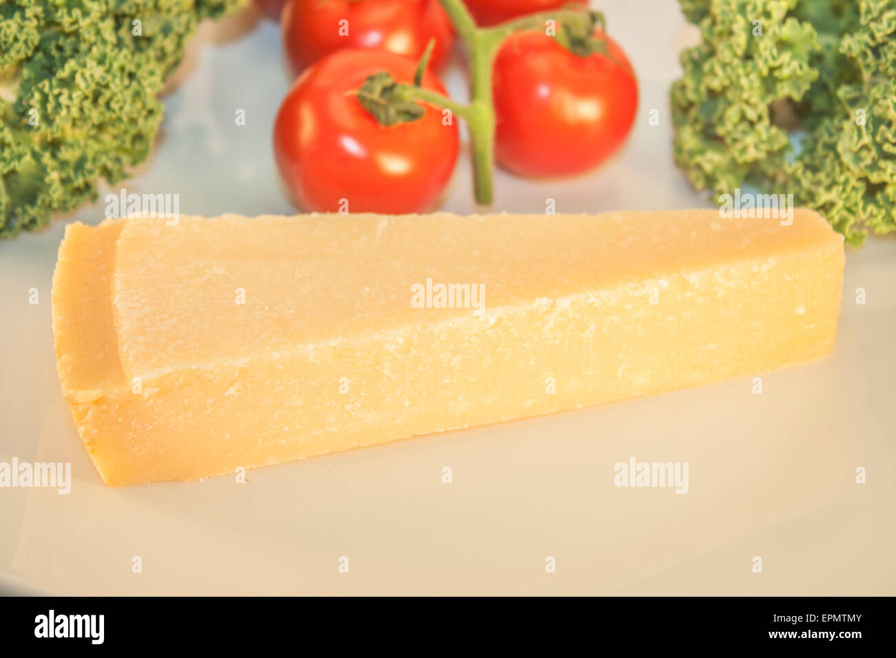 A parmesan wedge, in front of tomatoes and kale Stock Photo