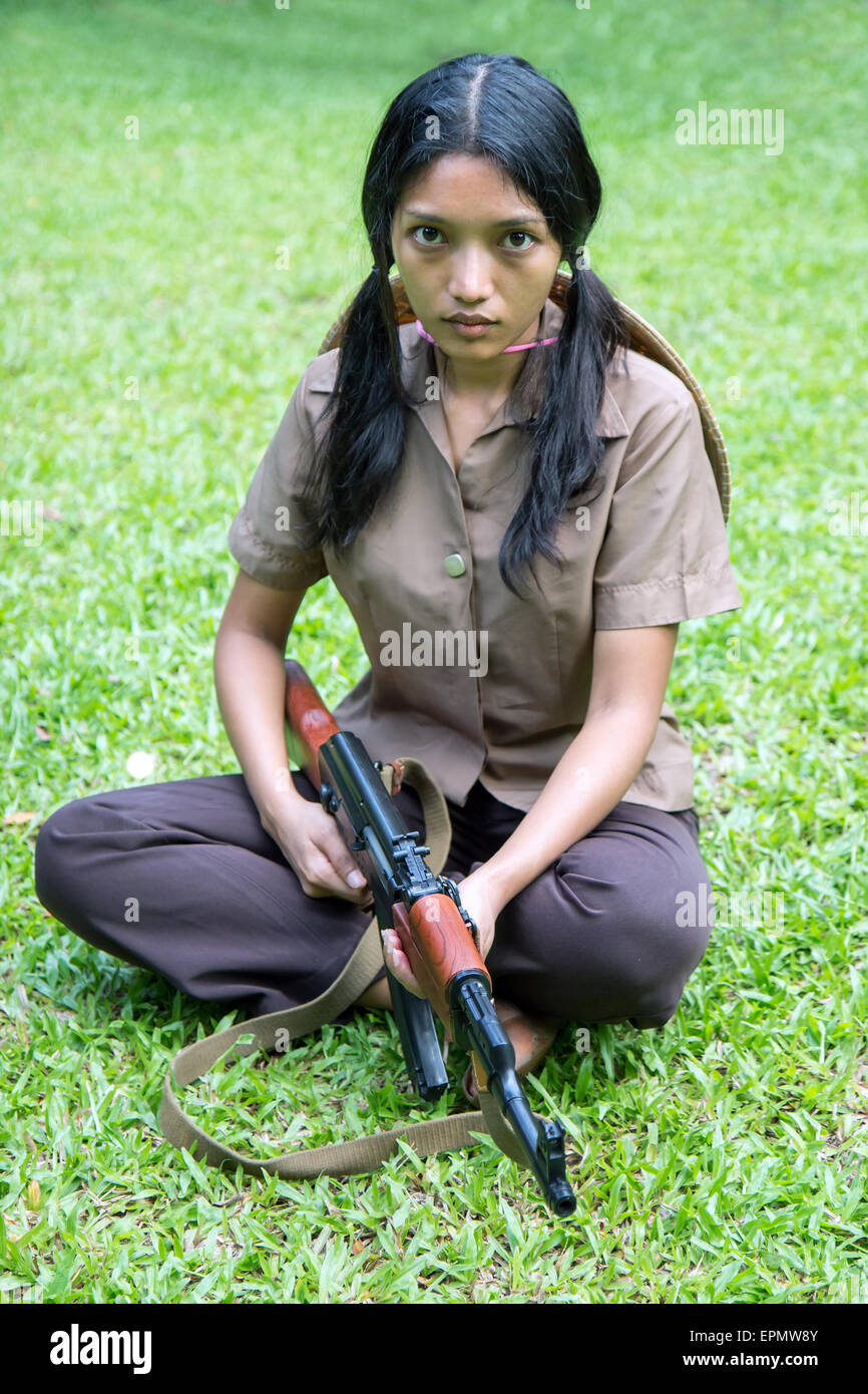 Asian woman with a machine gun sits on grass Stock Photo
