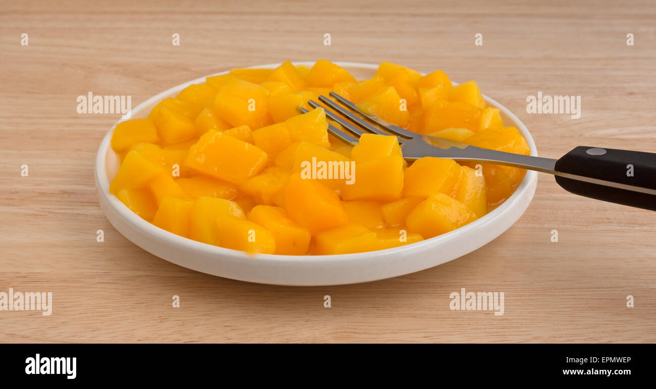 A serving of canned diced mangoes in a small dish with a black handle fork on a wood table top. Stock Photo