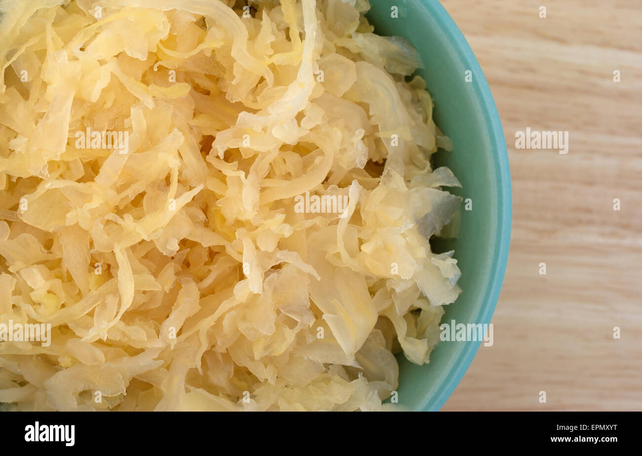 Close top view of a small bowl filled with canned sauerkraut on a wood table top. Stock Photo
