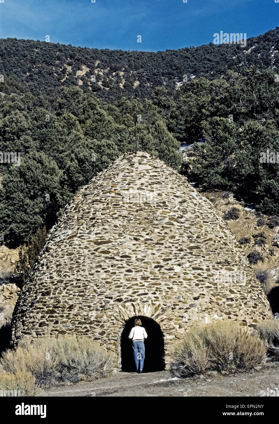 A tourist inspects one of the historic beehive-shaped charcoal kilns built in 1877 to make charcoal for ore smelters used in silver and lead mining operations nearby Death Valley, California, USA. The rock and mortar structures were constructed in Wildrose Canyon in the Panamint Mountains near sources of wood that included pine and juniper trees, which were slowly burned for a week to create the charcoal. The 10 kilns were abandoned when the mines shut down but were restored a century later and have become an attraction in Death Valley National Park. Stock Photo