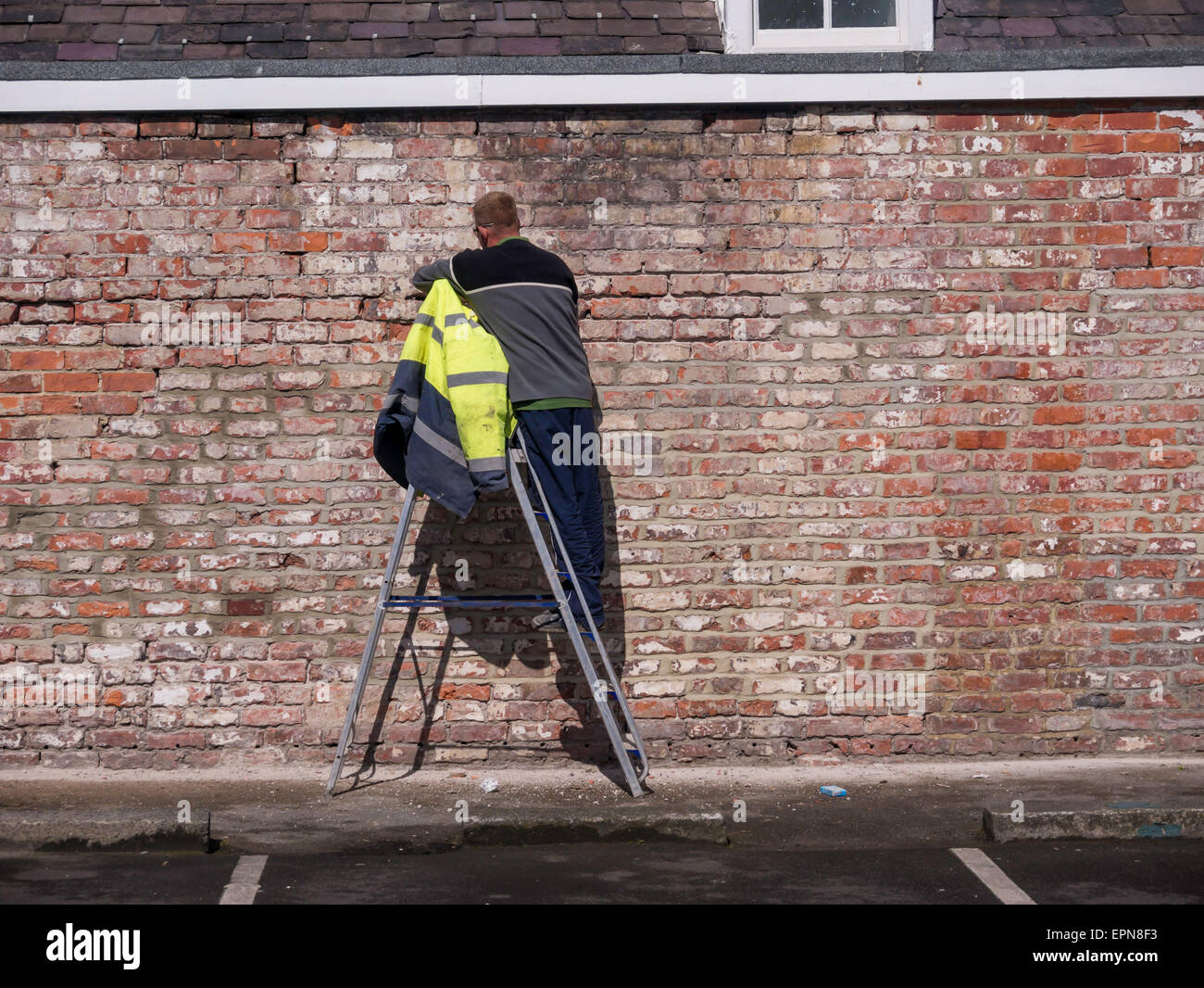 Workman using a hammer and cold chisel to  rake out old mortar from a brick wall prior to re-pointing and later rendering Stock Photo