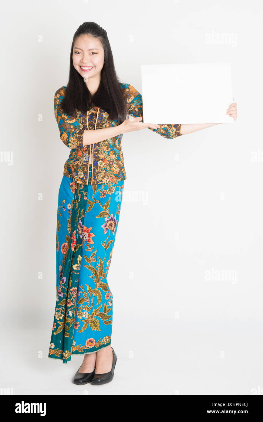 Full body portrait of Southeast Asian girl in batik dress hands holding  white blank card, standing on plain background Stock Photo - Alamy