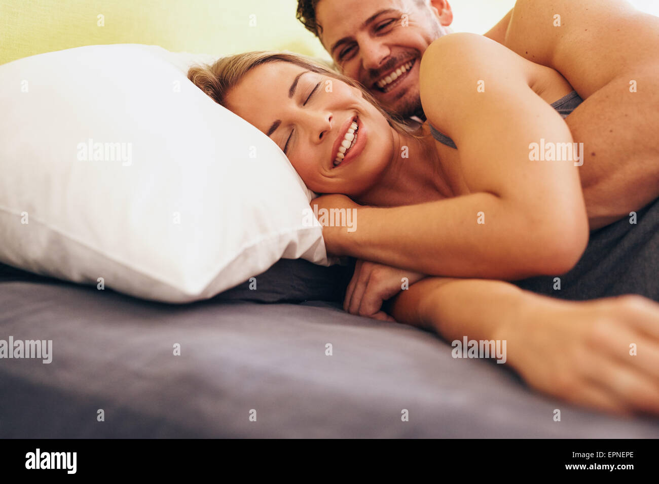 Happy young couple embracing while lying next to each other on bed. Caucasian couple smiling in bed together. Couple waking up. Stock Photo