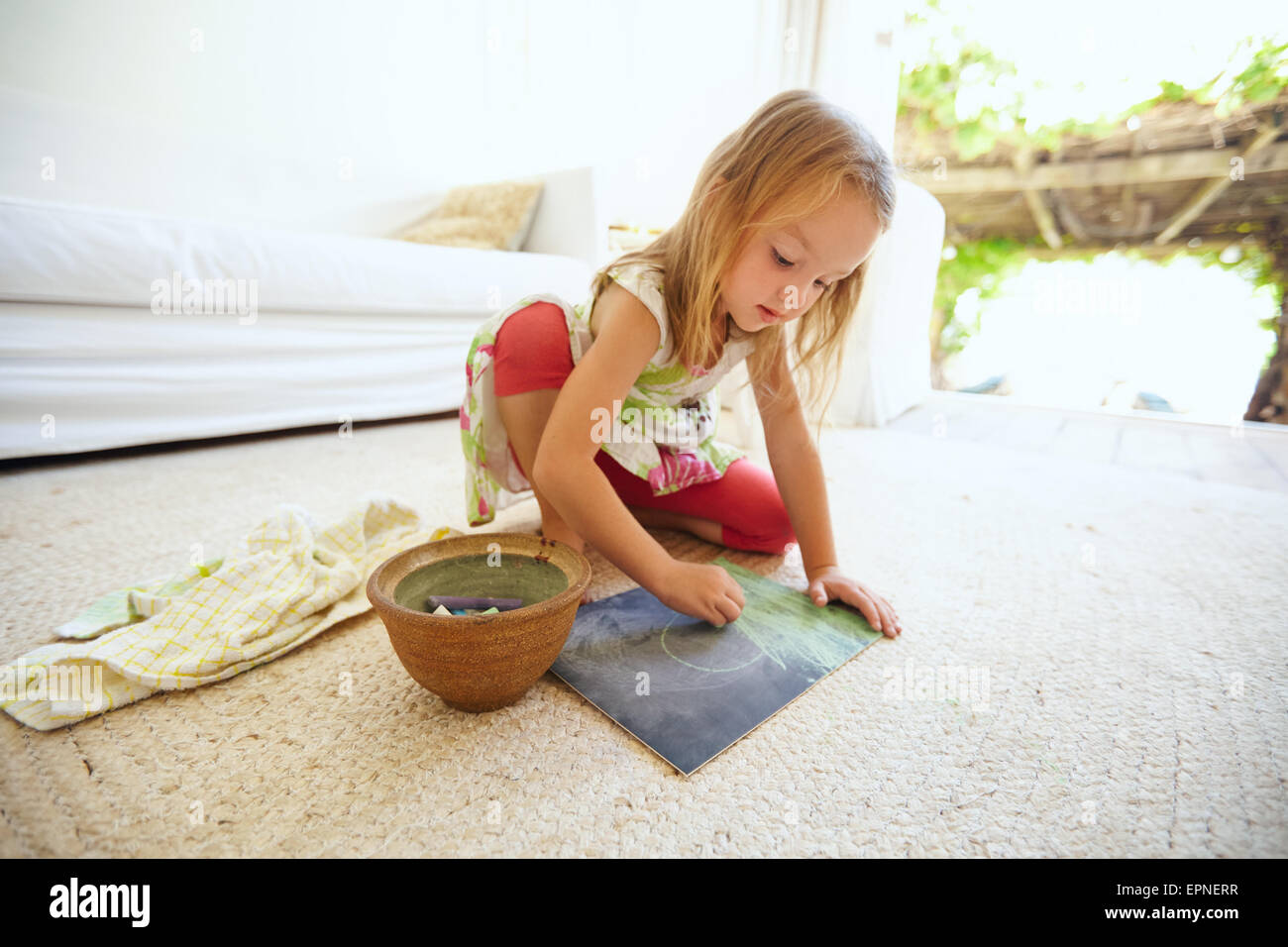 Shot of innocent little caucasian girl sitting on floor coloring a picture with color chalks. Schoolgirl drawing at home Stock Photo