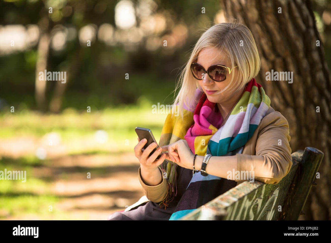 Young woman with smartphone in hands sitting on bench in the Park. Stock Photo