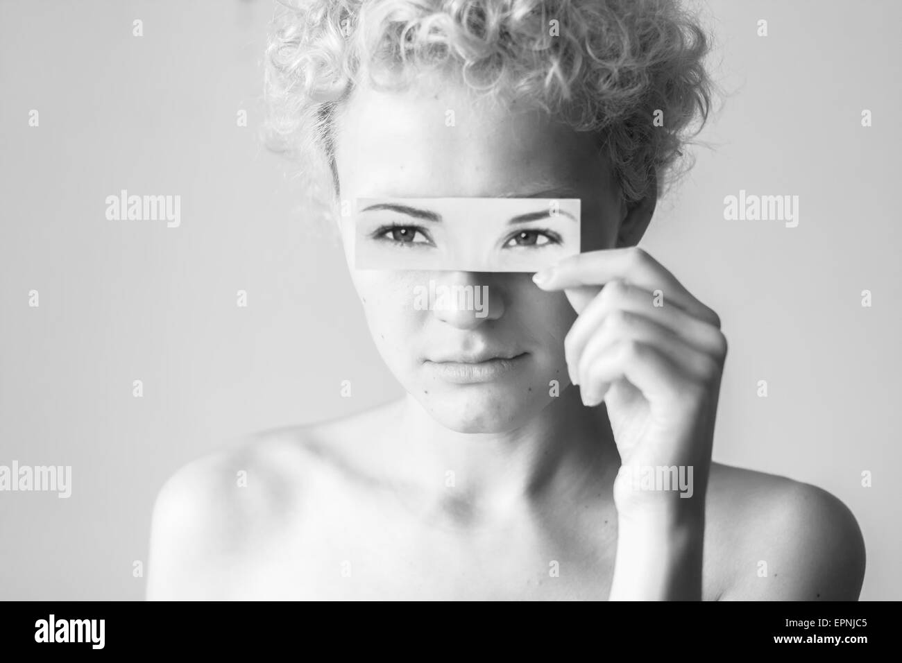 Tender curly-haired girl closes her eyes to picture painted eyes. Black and white photography in bright colors. Stock Photo