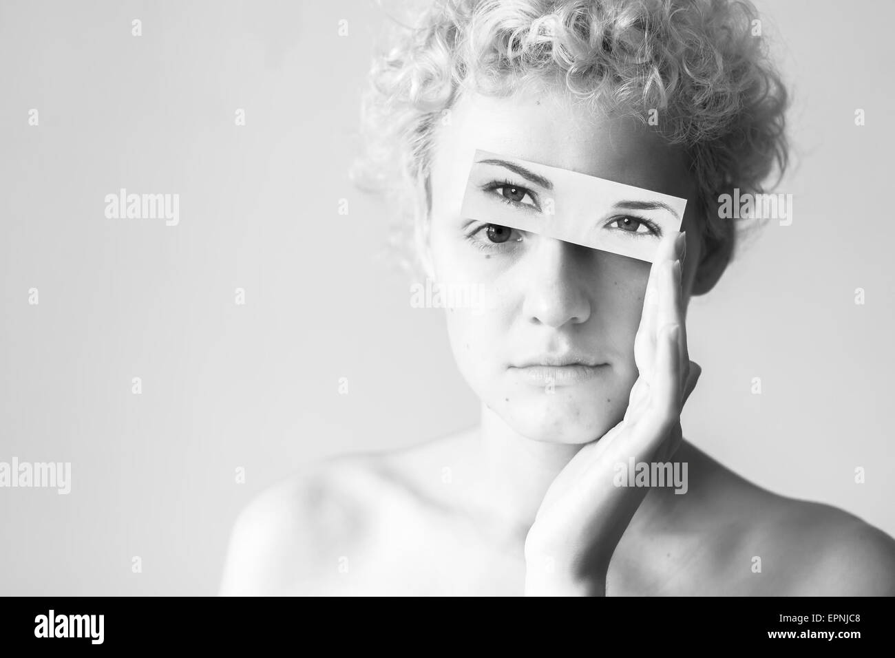 Young curly-haired tender girl closes her eyes to picture painted eyes. Black and white photography in bright colors. Stock Photo