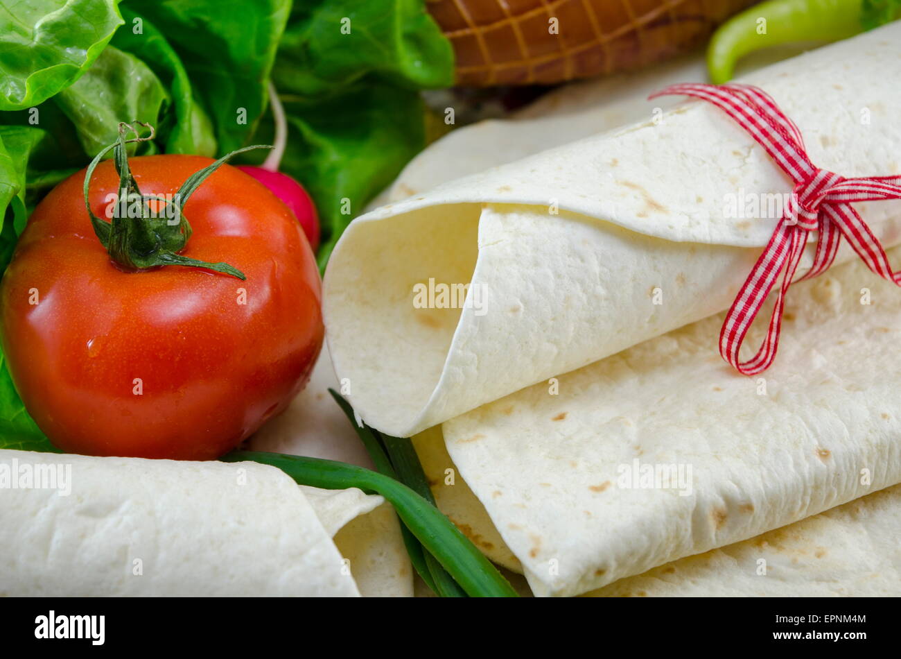 Empty tortillas tied with a red ribbon on a table with tomato, lettuce and ham Stock Photo
