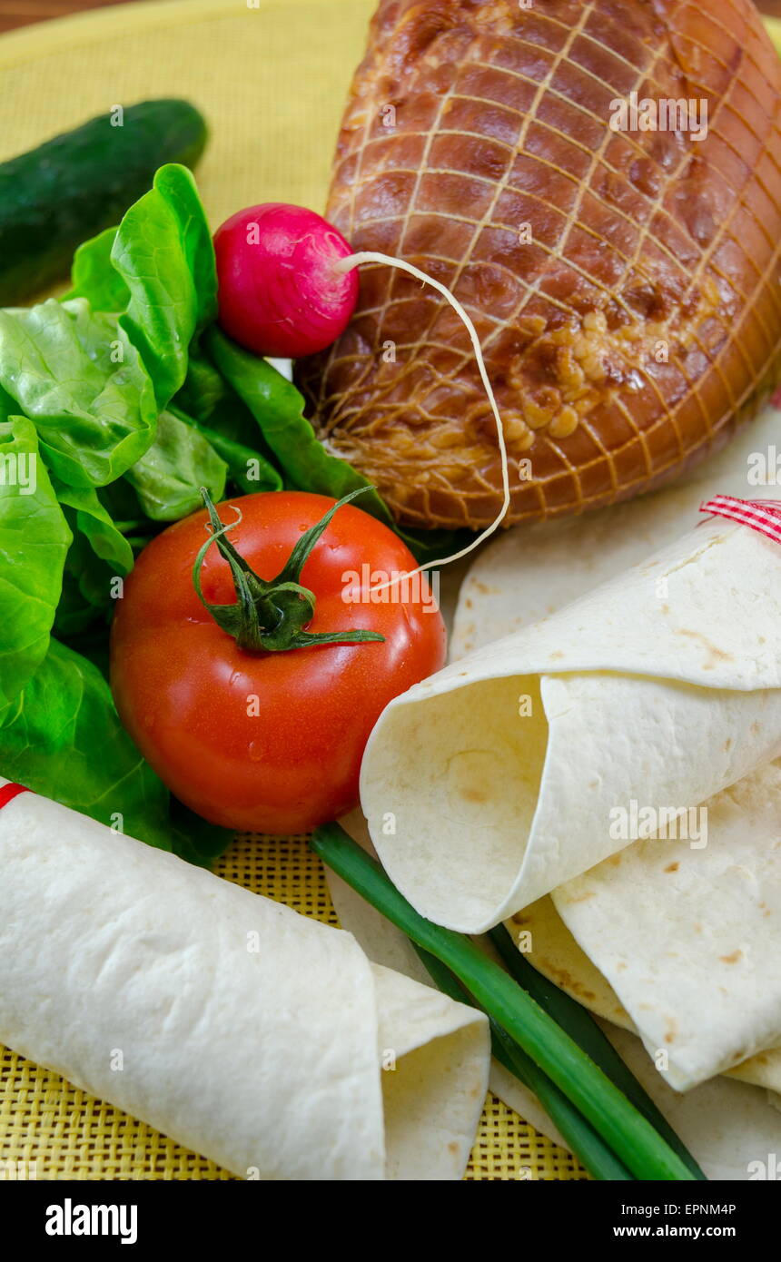 Empty tortillas tied with a red ribbon on a table with tomato, lettuce and ham Stock Photo