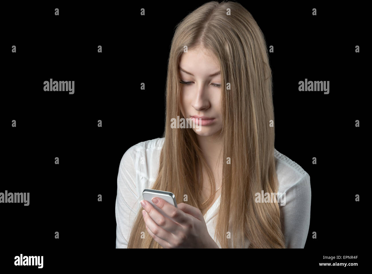 Attractive young girl feels depressed after reading bad sms on her mobile cellular phone. Isolated on black. Stock Photo
