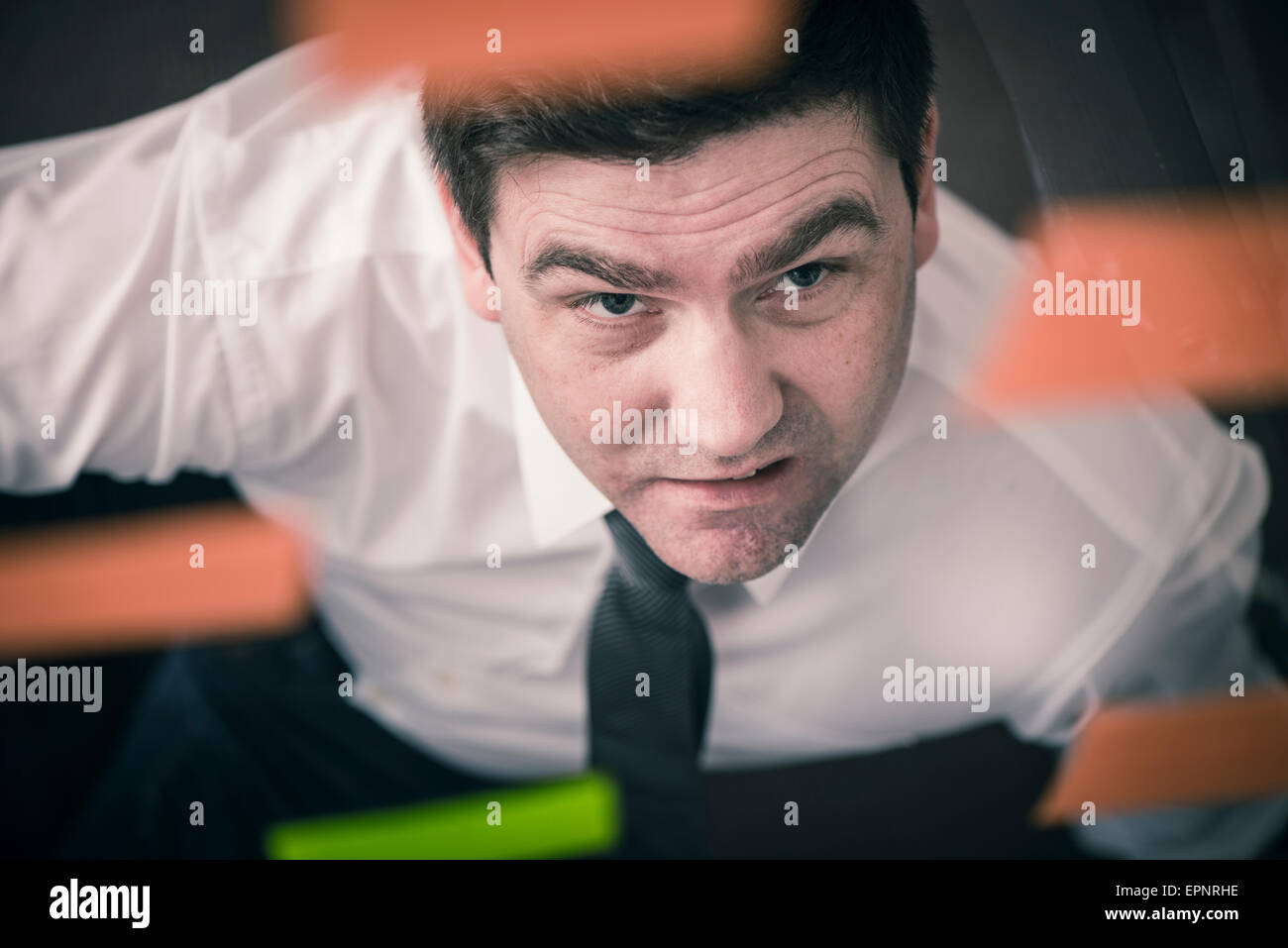 Businessman looking up at glass wall with adhesive notes. Conceptual