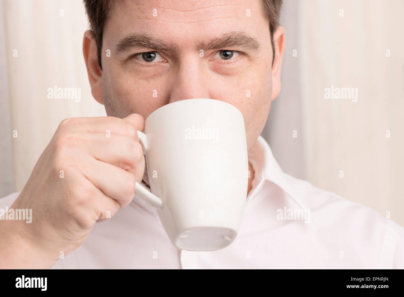 Close up of man drinking from coffee cup and looking in camera. Stock Photo