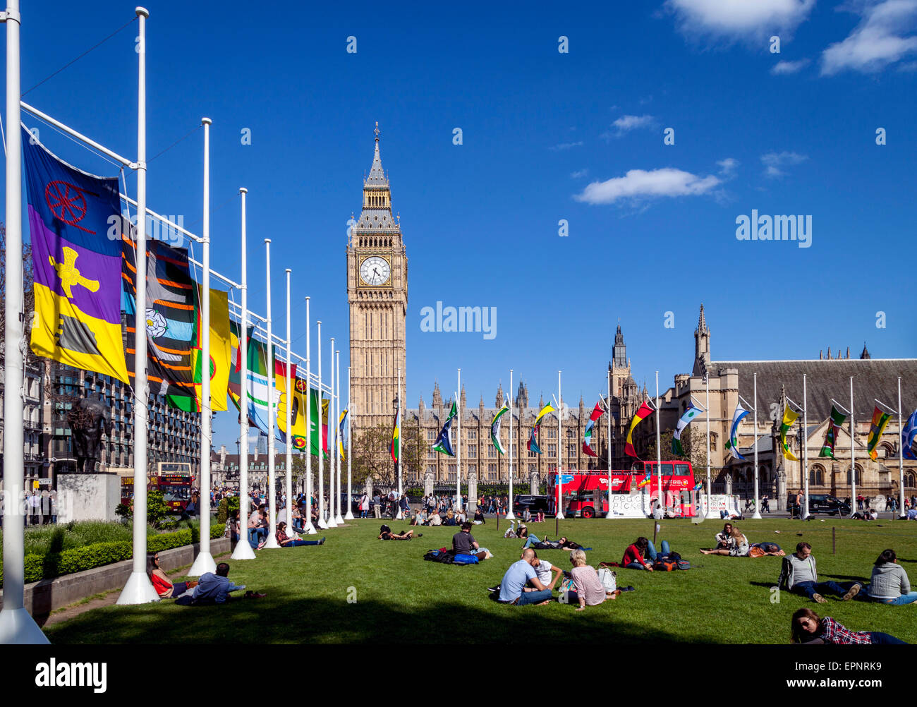 Tourists Sitting In The Sunshine In Parliament Square In Front of The Houses of Parliament , London, England Stock Photo
