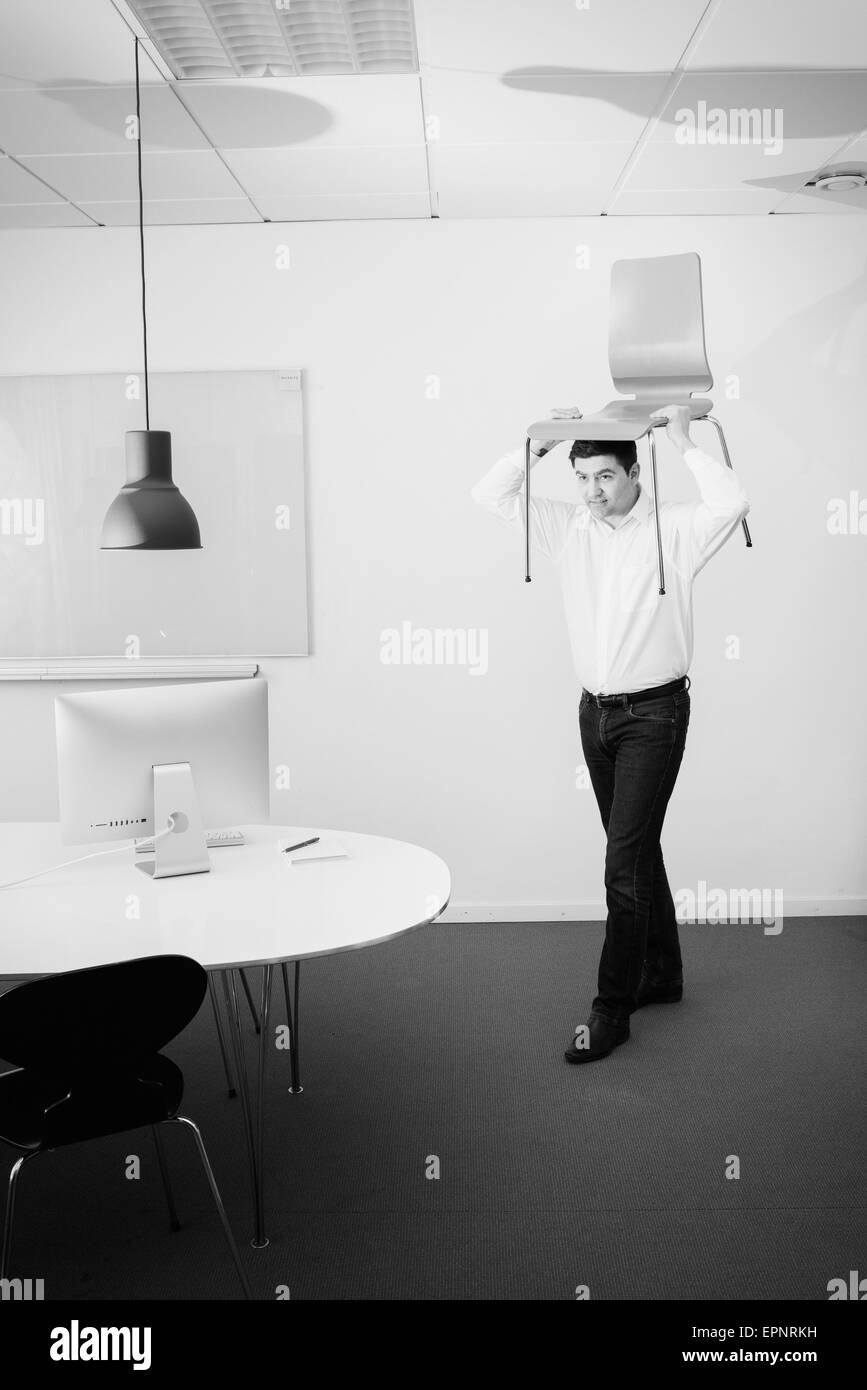 Businessman carrying chair on his head. Conceptual image of business relocation, startup or change. Stock Photo