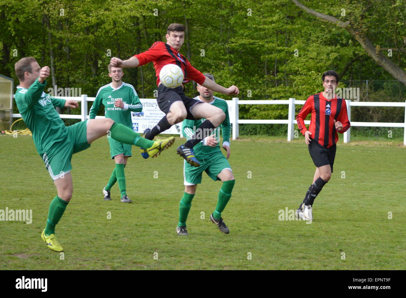 Footballer jumps high to get the ball in a local amateur football match Stock Photo