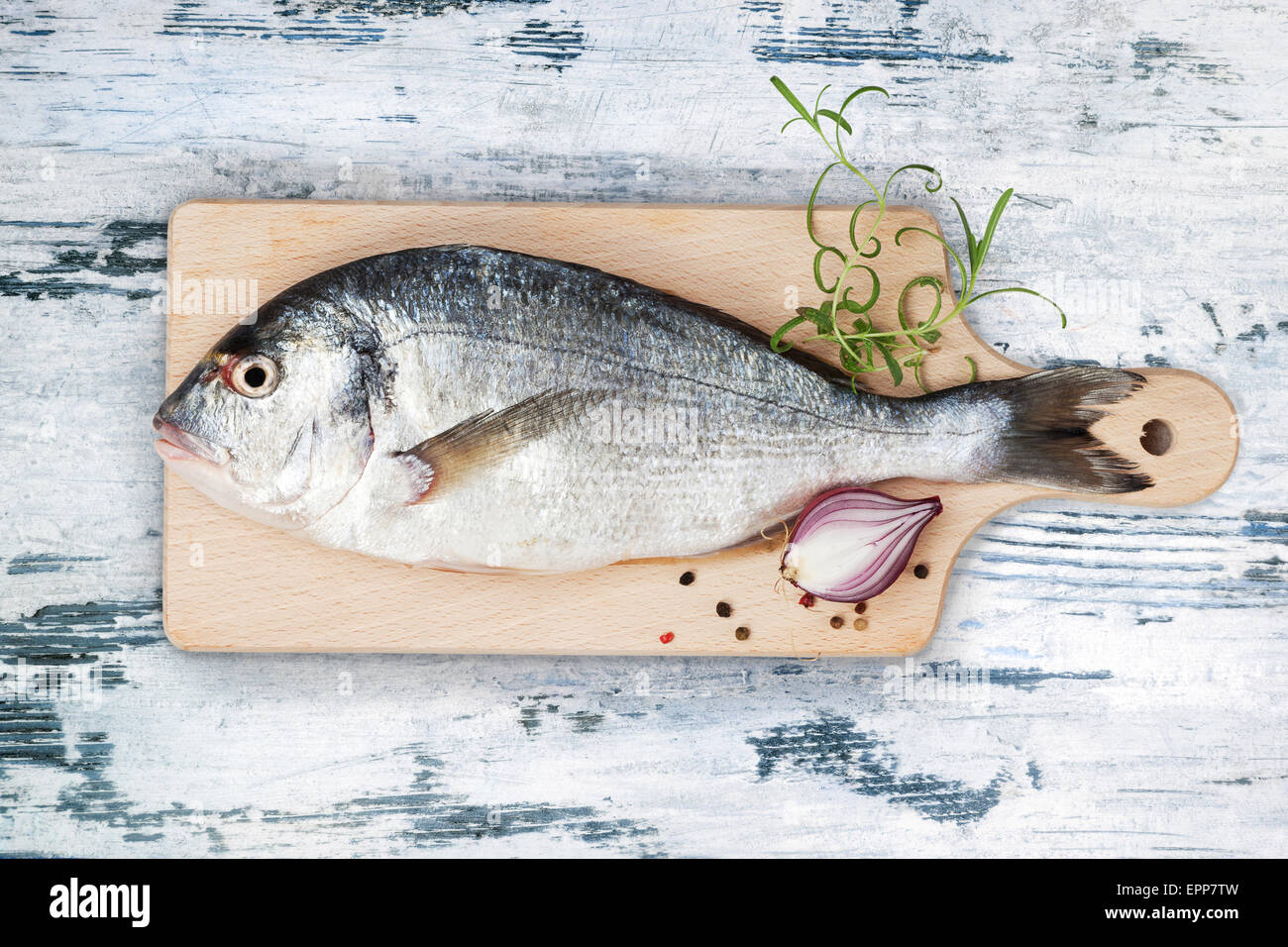 Delicious fresh sea bream fish on wooden kitchen board with onion, rosemary and colorful peppercorns on wooden board Stock Photo