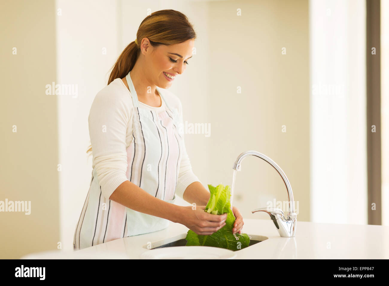 happy young woman washing lettuce in the kitchen Stock Photo