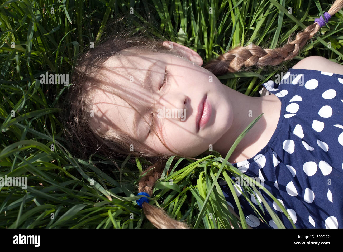 young pretty caucasian girl with two pigtail braids lying and sleeping on green grass Stock Photo