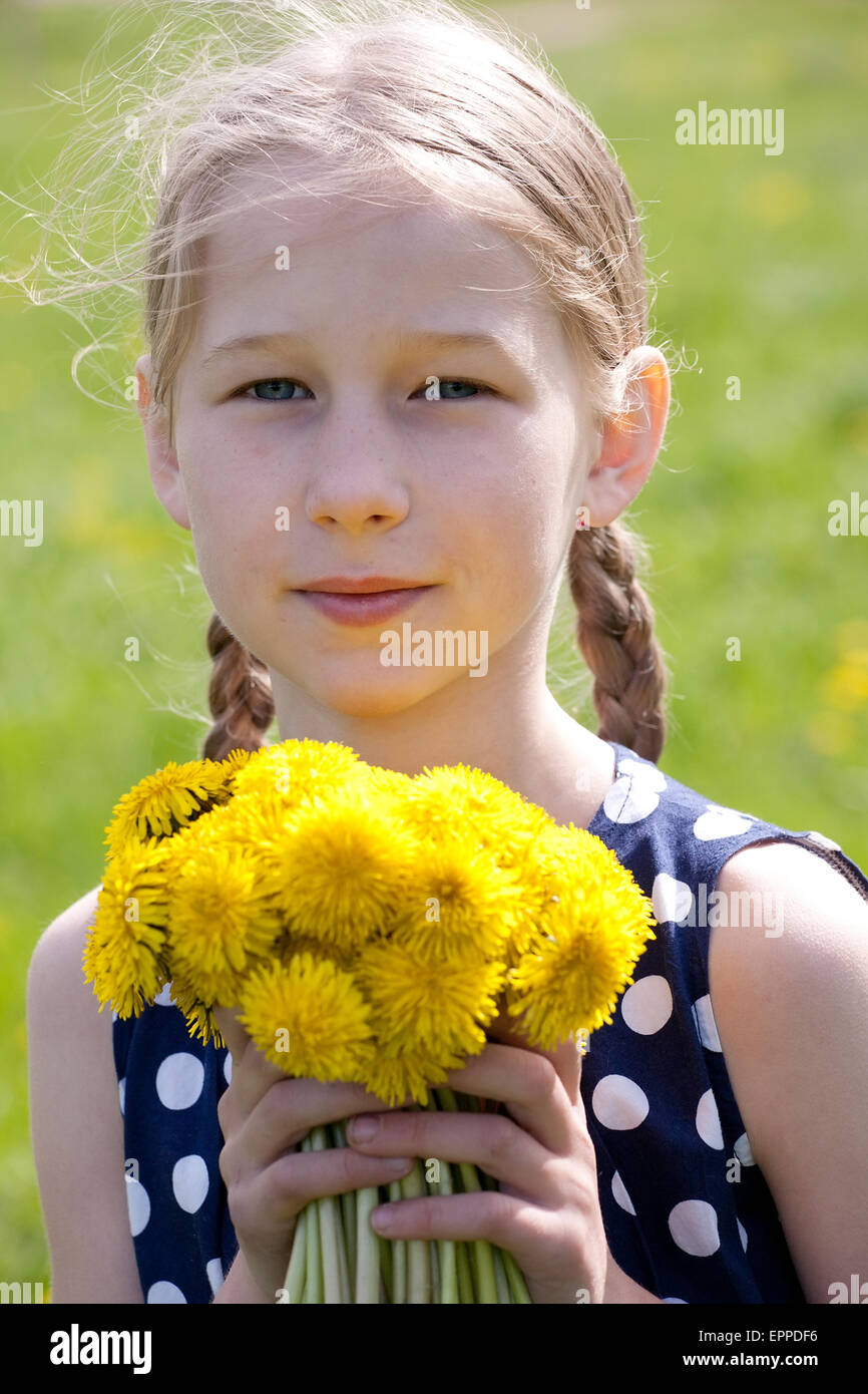 young pretty caucasian girl standing with yellow dandelions in hands, face closeup Stock Photo