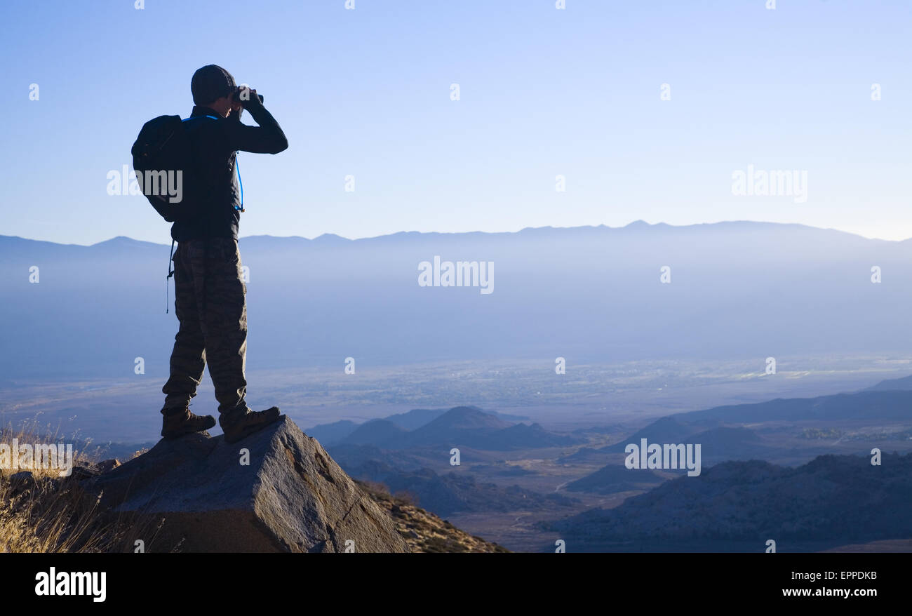 Hiker surveys his surroundings through binoculars. Stock Photo