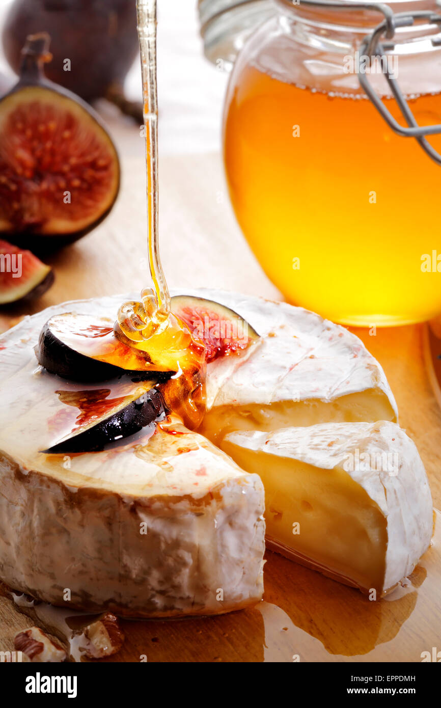 Brie Cheese and sliced Figs poured with honey on wood cheese-board Stock Photo