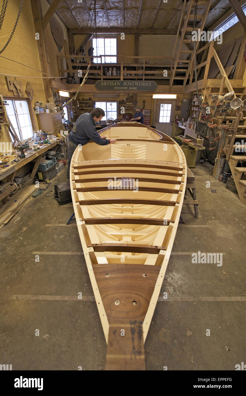 A boat builder, works on the boat he is restoring in a boatbuilding shed. Stock Photo