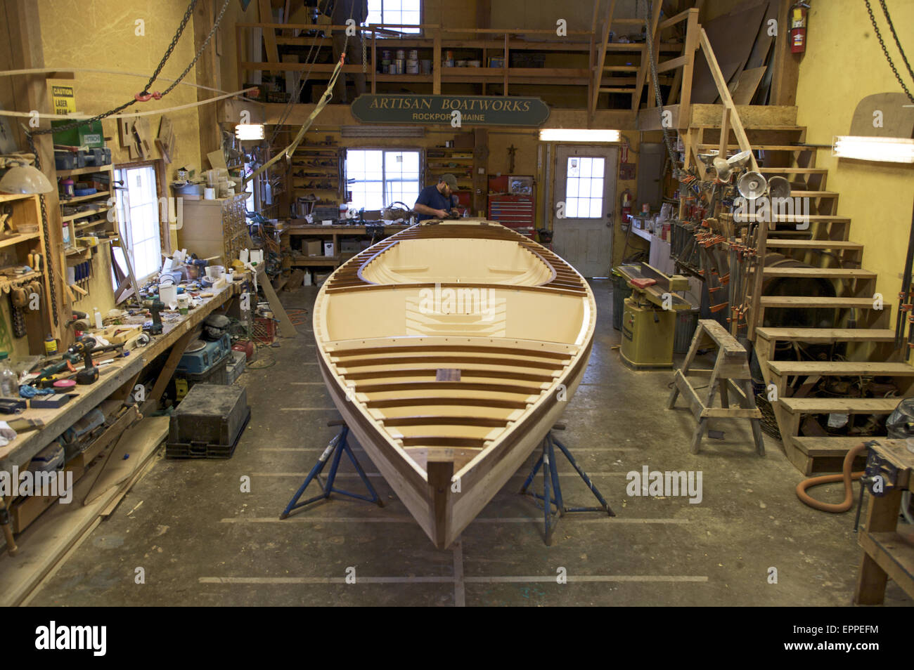 A boat builder, works on the boat he is restoring in a boatbuilding shed. Stock Photo