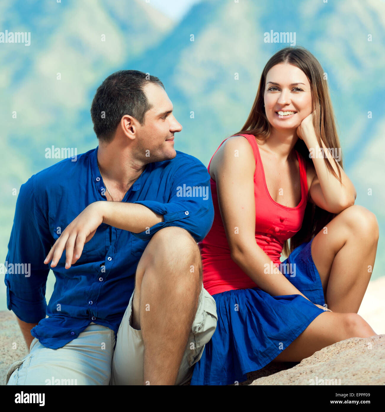 Attractive couple sitting on the cliff. Mountain on background Stock Photo