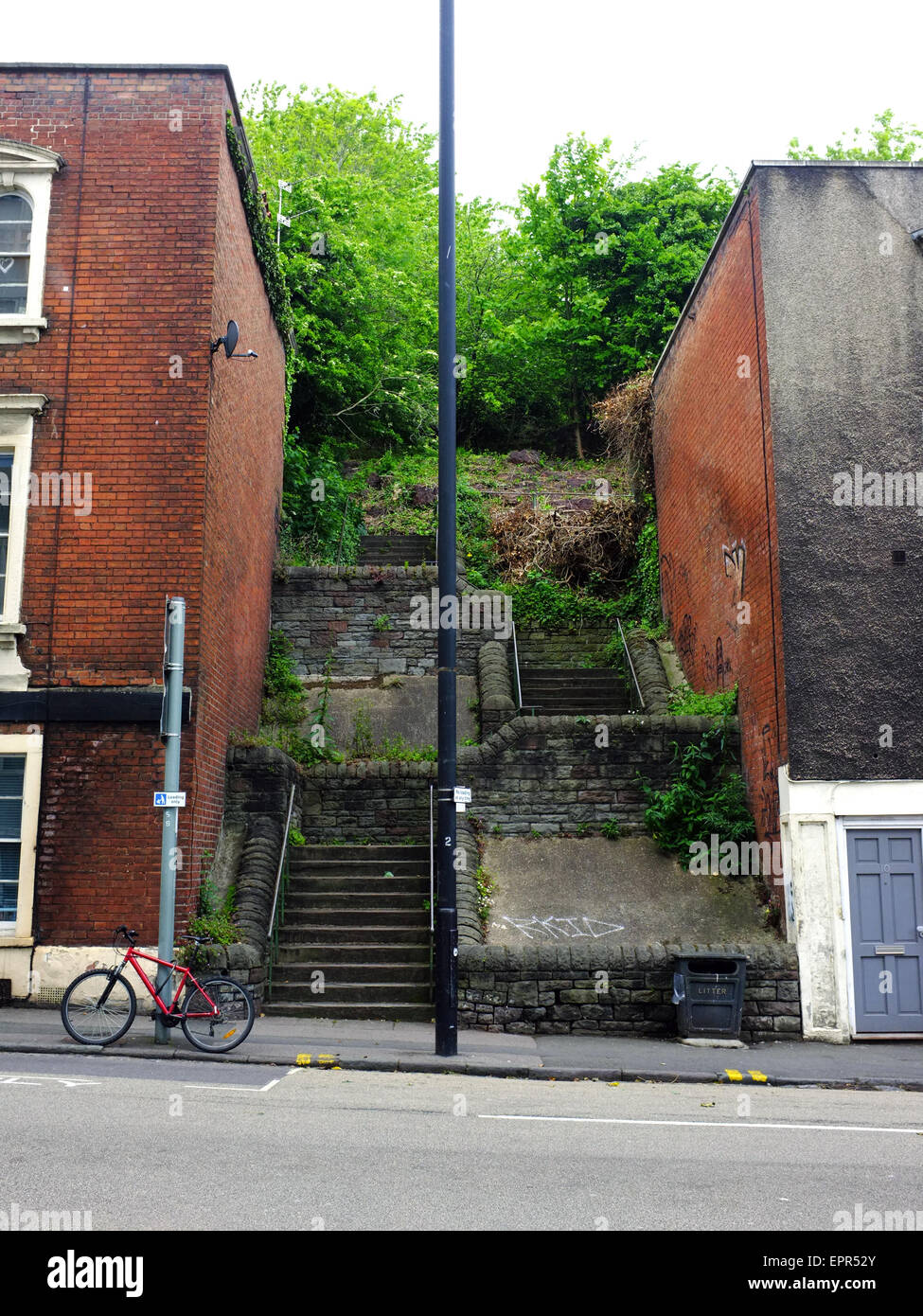 A red bicycle parked by a set of steps winding up a slope between two buildings in Bristol. Stock Photo