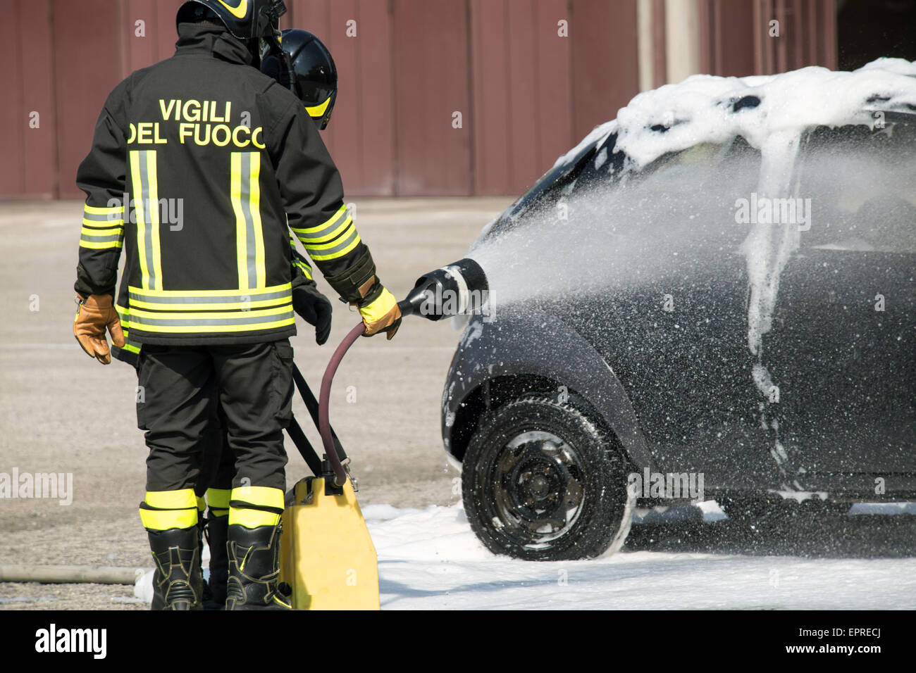 two firefighters in action with foam to put out the fire of the car Stock Photo