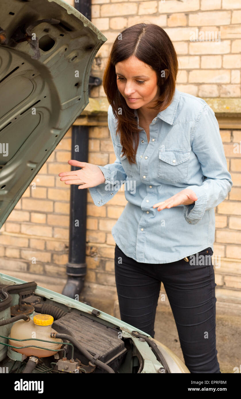 young woman looking annoyed at the engine of her car Stock Photo