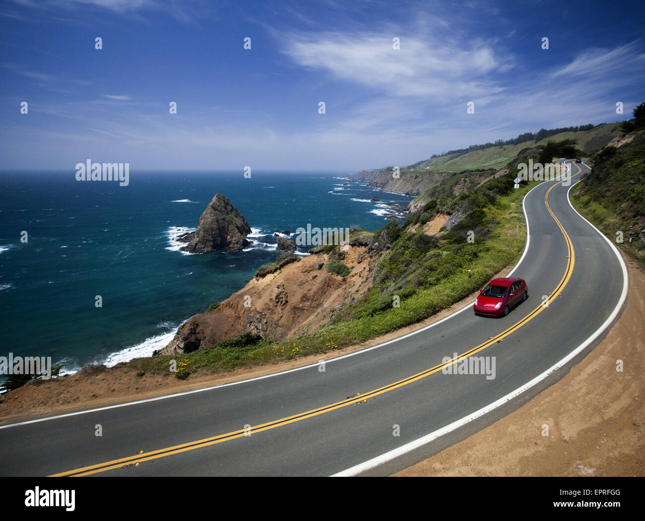 A red car drives on a highway near the ocean. Stock Photo