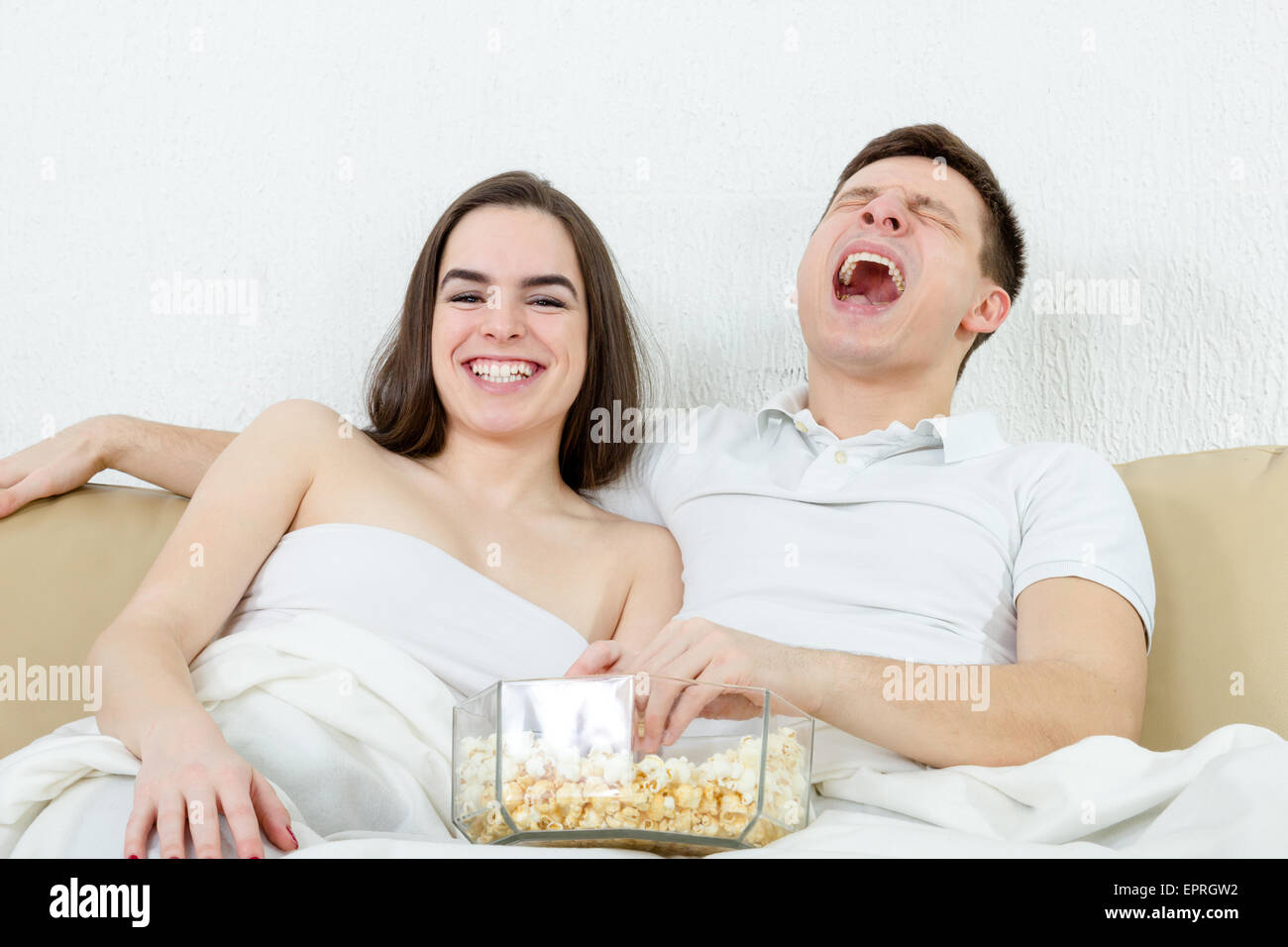 Happy young attractive couple sitting on the couch in living room at home covered with blanket and watch fanny comedy on televis Stock Photo