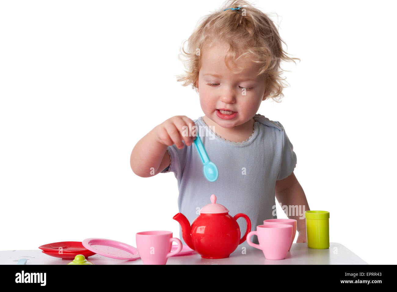 Two year old blond girl playing with a colourful plastic tea set on white background Stock Photo