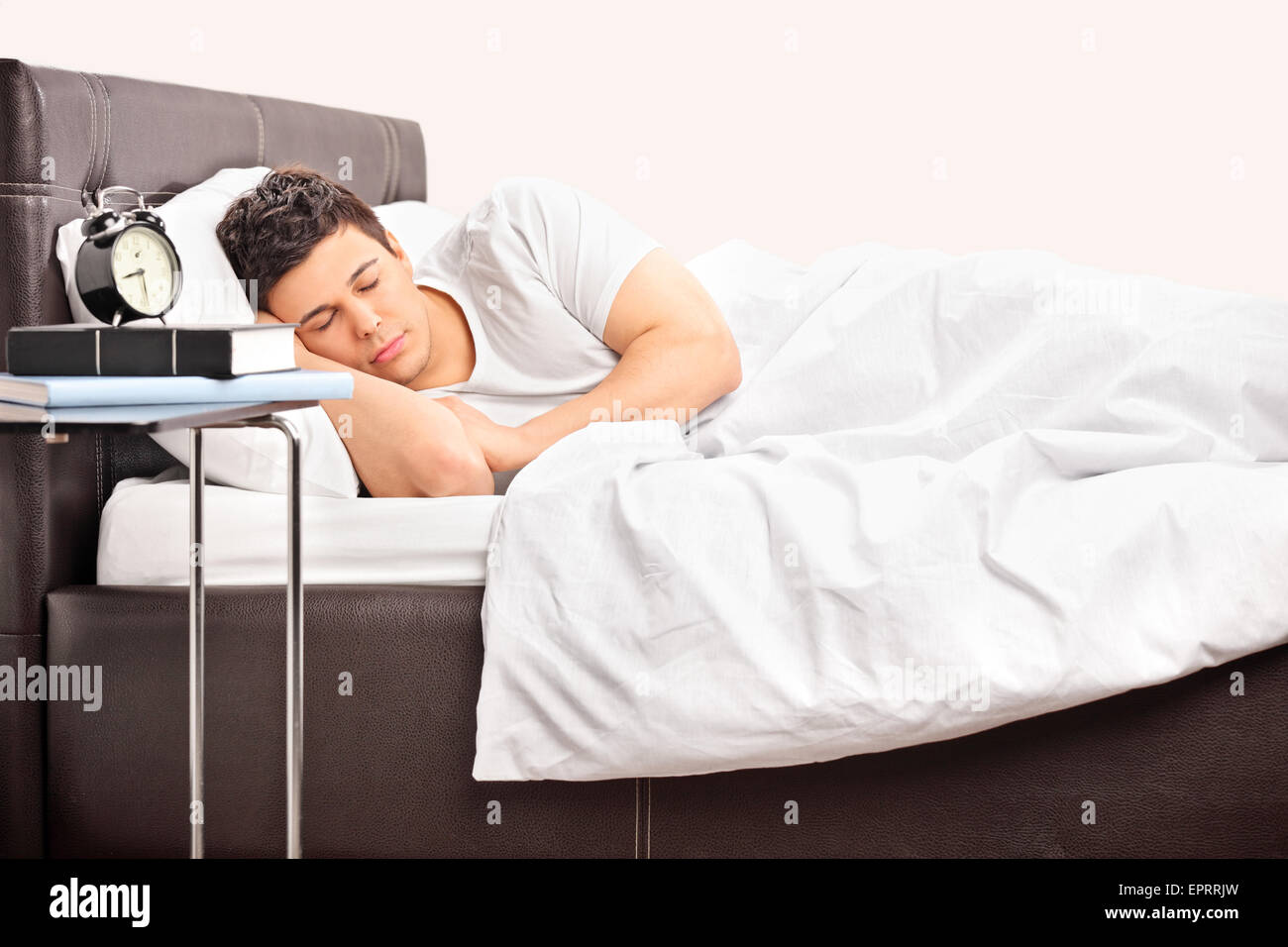Young man sleeping on a comfortable bed covered with a white blanket in a bedroom Stock Photo
