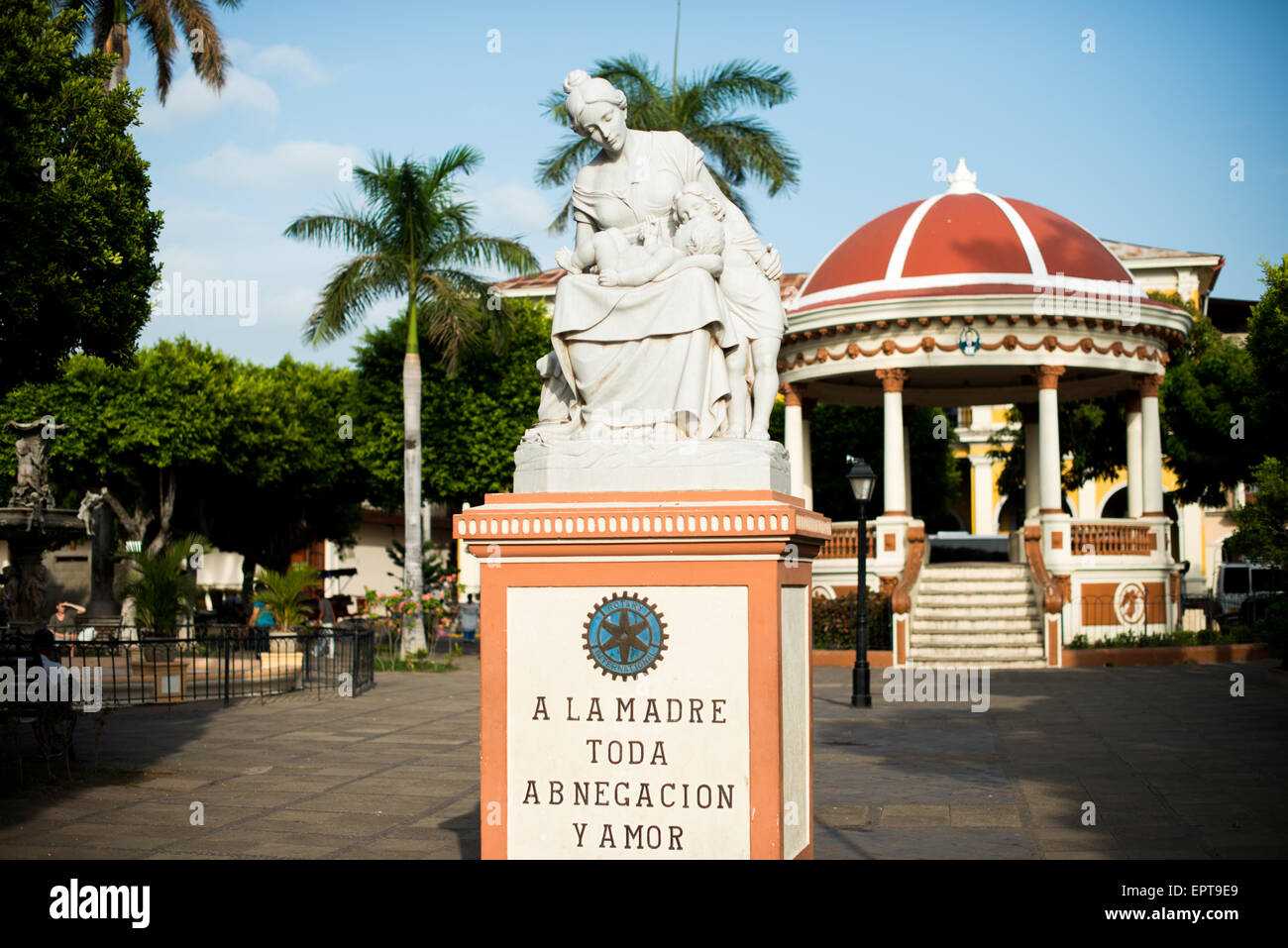 Motherhood Statue Parque Central Granada Nicaragua // GRANADA, Nicaragua — A statue honoring motherhood stands prominently in Parque Central, the main square and historic heart of Granada. The monument features an inscription that reads 'Mother of all devotion and love,' celebrating maternal dedication. Parque Central serves as a central gathering place for locals and visitors in Granada, one of Nicaragua's oldest colonial cities. The square is surrounded by colorful Spanish colonial architecture and important civic buildings. This public artwork represents one of many cultural monuments found Stock Photo