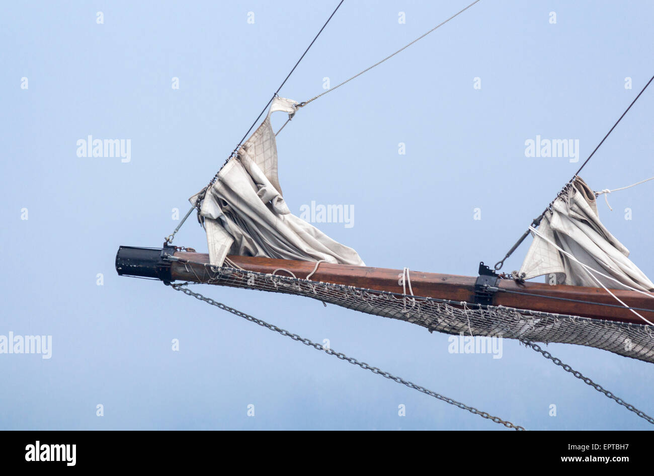 Tall ship mast with sails down against a bright blue sky. Stock Photo