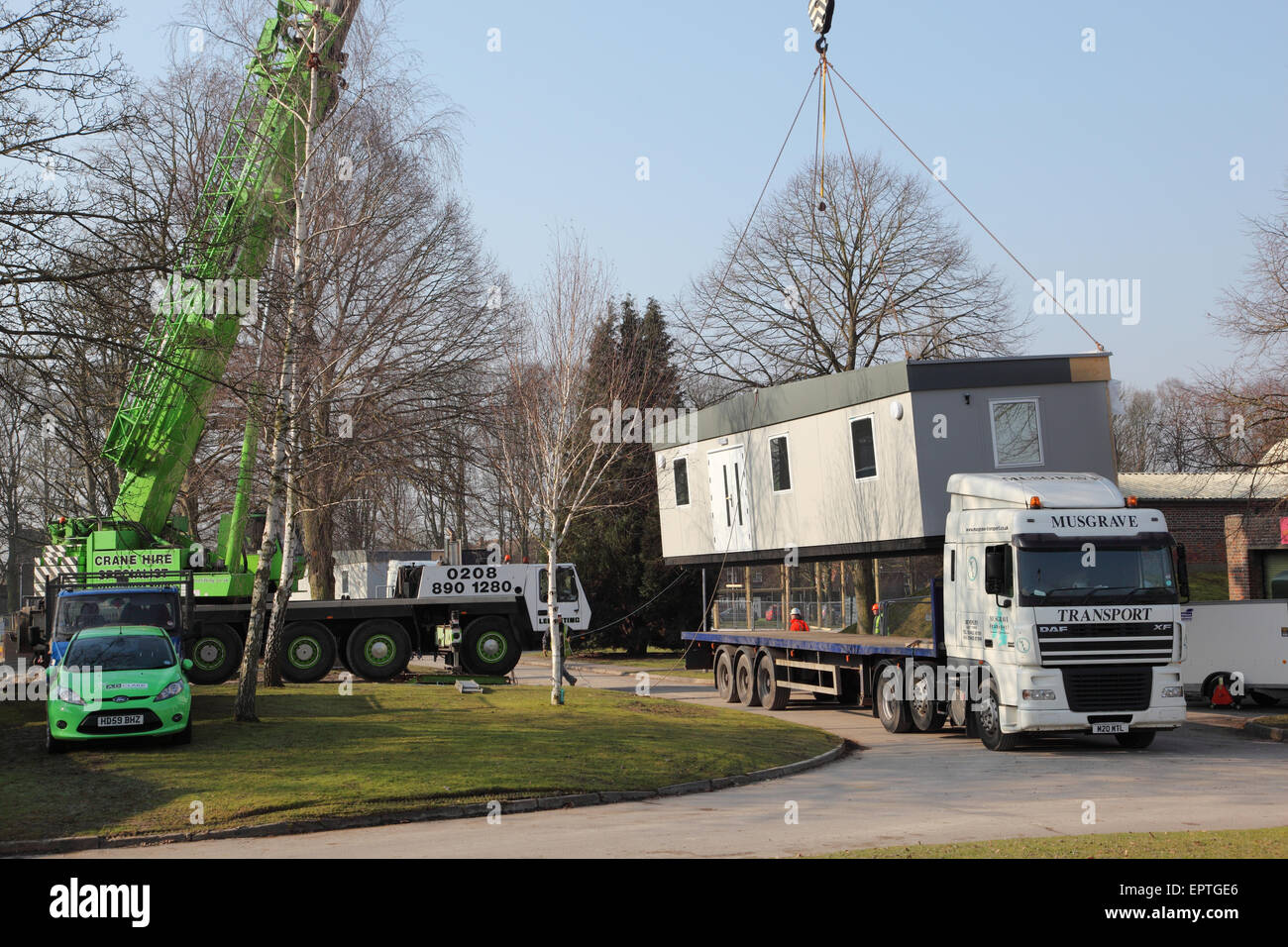 A section of a modular building is lifted from an articulated lorry by a mobile crane during installation Stock Photo