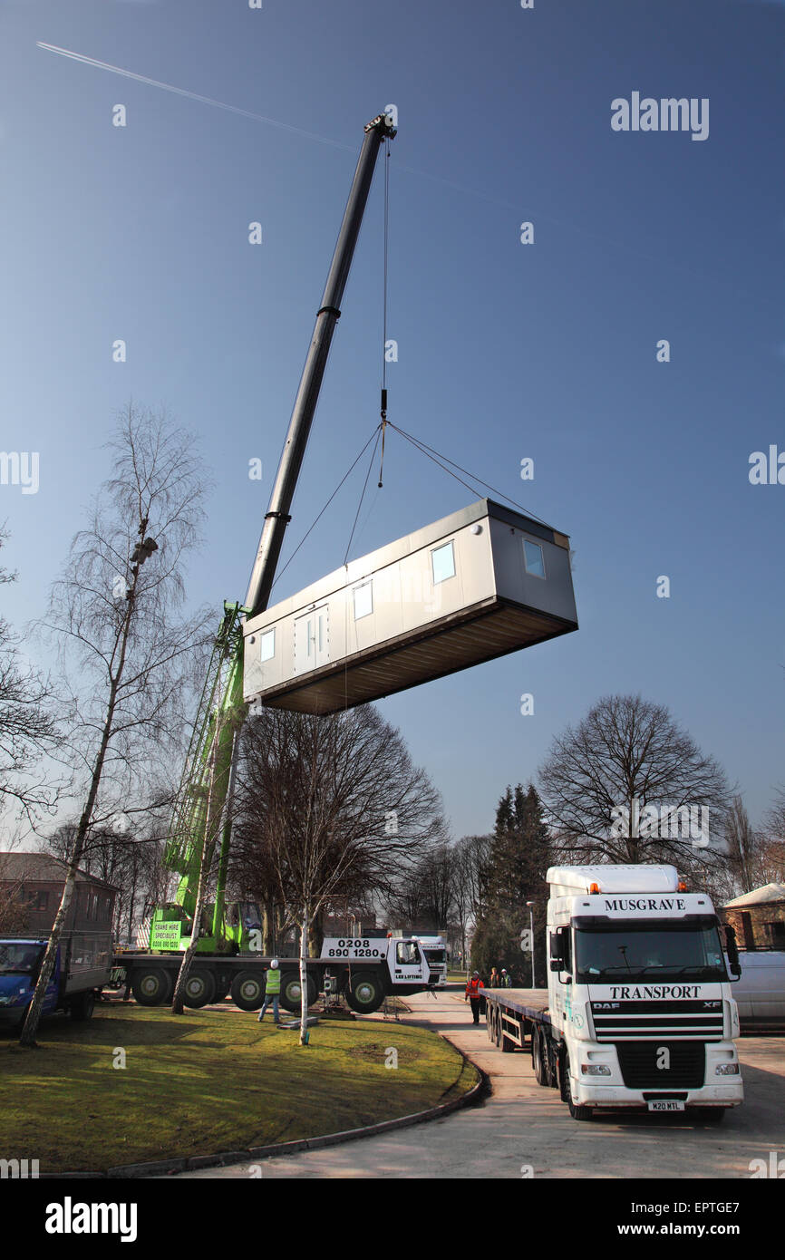 A section of a modular classroom building is lifted from an articulated lorry by a mobile crane during installation Stock Photo